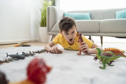 Junge schreit beim Spielen mit Spielzeugtieren auf dem Teppich im Wohnzimmer - SNF00451