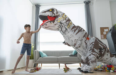 Shirtless boy fighting with large toy dinosaur in living room - SNF00456