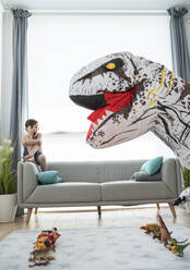 Hemdloser Junge schreit beim Betrachten eines großen Spielzeugdinosauriers im Wohnzimmer - SNF00457