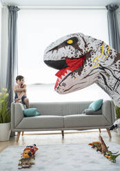 Shirtless boy screaming while looking at large toy dinosaur in living room - SNF00457