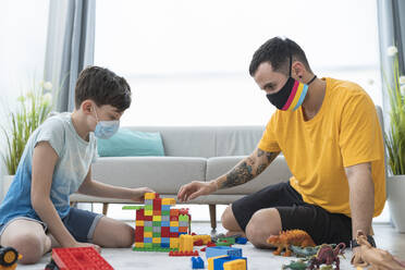 Mann mit Maske spielt während der Quarantäne mit einem Jungen im Wohnzimmer seines Hauses - SNF00468