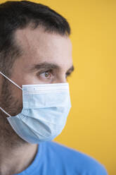 Close-up of thoughtful mid adult man wearing mask against yellow background - SNF00480