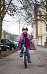 Smiling girl wearing helmet riding bicycle on street in city - JFEF00951