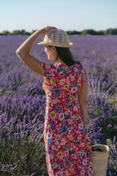 Woman wearing floral dress standing in vast lavender field - GEMF03973
