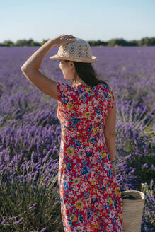Frau in geblümtem Kleid steht in einem weiten Lavendelfeld - GEMF03973