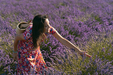 Beautiful woman touching lavender blooming in field - GEMF03980