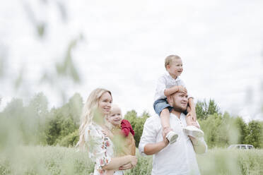 Smiling parents carrying children while standing against clear sky in oats field - EYAF01243