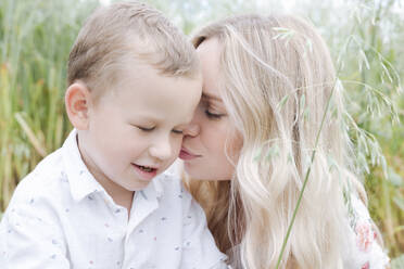 Close-up of young woman kissing cute son while sitting in oats field - EYAF01249