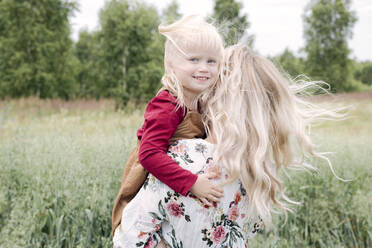 Junge Frau mit blondem Haar trägt ihre niedliche Tochter in einem Haferfeld - EYAF01253