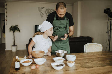 Vater und Tochter backen Kekse und benutzen ihr Smartphone zu Hause - GMLF00419