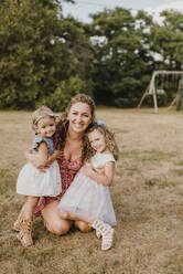 Happy mother hugging daughters on a meadow - SMSF00069