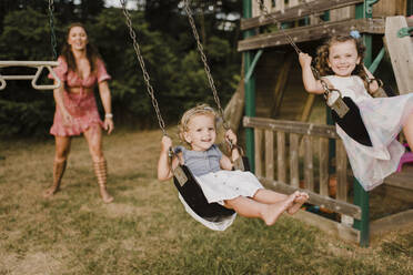 Happy girls on a swing with mother in background - SMSF00074