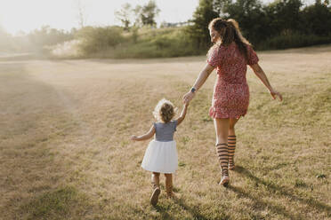 Mutter und Tochter spazieren auf einer Wiese im Gegenlicht - SMSF00079