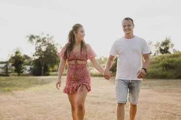 Glückliches Paar spaziert Hand in Hand auf einer Wiese - SMSF00090
