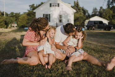 Parents with two daughters sitting on a meadow in front of their home - SMSF00100