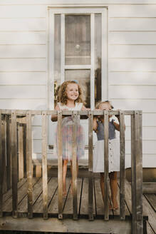 Zwei glückliche Schwestern stehen auf der Veranda ihres Hauses - SMSF00103