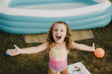 Porträt eines glücklichen Mädchens am aufblasbaren Schwimmbecken im Garten - SMSF00113