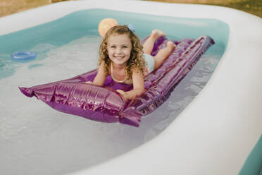 Porträt eines glücklichen Mädchens auf einer Luftmatratze in einem aufblasbaren Schwimmbecken - SMSF00116