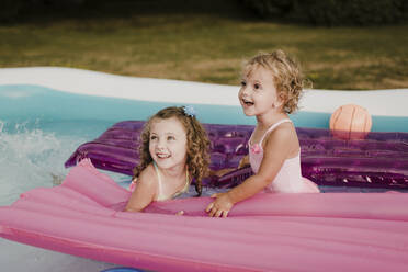 Zwei glückliche Mädchen mit Luftmatratze in einem aufblasbaren Schwimmbad - SMSF00117
