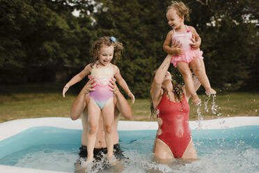 Happy family playing in an inflatable swimming pool in garden - SMSF00121