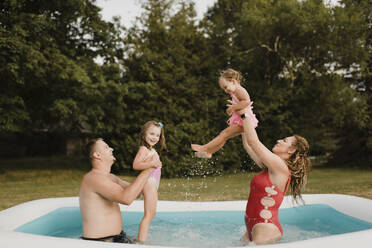 Happy family playing in an inflatable swimming pool in garden - SMSF00122