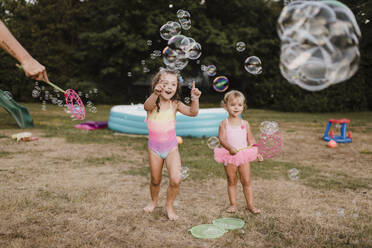 Zwei glückliche Mädchen spielen mit Seifenblasen im Garten - SMSF00137