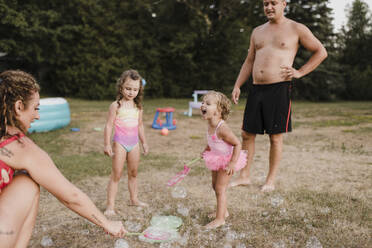 Glückliche Familie spielt mit Seifenblasen im Garten - SMSF00138