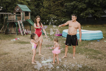 Happy family playing with soap bubbles in garden - SMSF00139