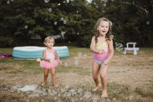 Two happy girls playing with soap bubbles in garden - SMSF00140