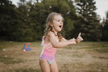 Happy girl playing with soap bubbles in garden - SMSF00141