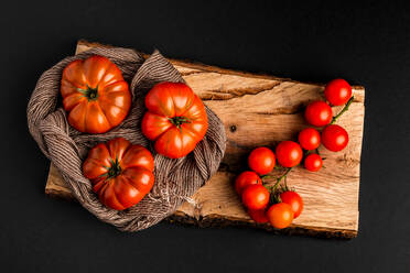 Frische reife Tomaten und Stoffserviette auf Stück Holz vor schwarzem Hintergrund platziert - ADSF09500