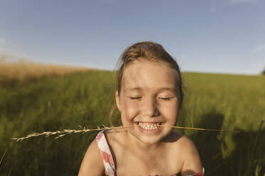 Close-up of smiling girl with eyes closed sitting on land against clear sky during sunset - KMKF01435