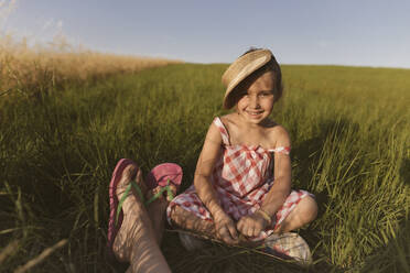Lächelndes Mädchen sitzt mit Mutter auf dem Land gegen den klaren Himmel bei Sonnenuntergang - KMKF01436