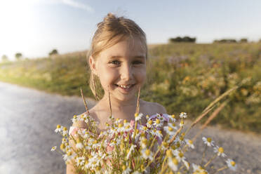 Nahaufnahme eines lächelnden Mädchens mit Blumen auf der Straße gegen den Himmel bei Sonnenuntergang - KMKF01437