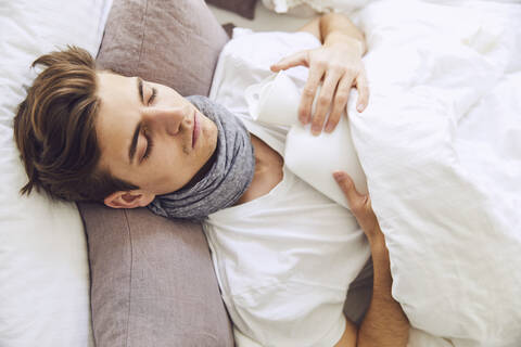 Nahaufnahme eines kranken jungen Mannes mit Wärmflasche, der zu Hause auf dem Bett schläft, lizenzfreies Stockfoto