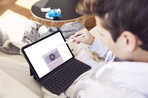 Nahaufnahme eines jungen Mannes, der auf dem Sofa zu Hause über einem digitalen Tablet recherchiert - UKOF00017