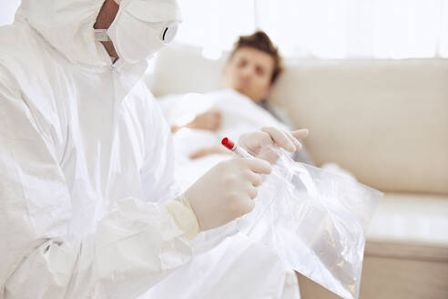 Close-up of doctor holding medical sample in plastic bag while patient resting on sofa - UKOF00032