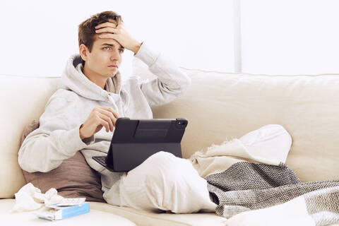 Young man with head in hands using digital tablet on sofa at home stock photo