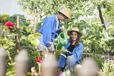 Female friends wearing hats watering plants in garden - UKOF00050