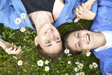 Close-up of cheerful female friends lying by flowers on grassy land in garden - UKOF00059