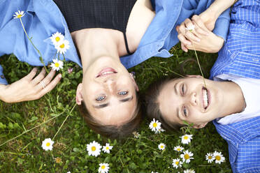 Close-up of smiling young friends lying on grassy land in garden - UKOF00060