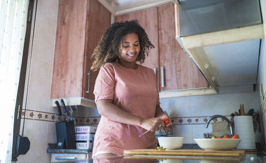 Lächelnde junge Frau beim Schneiden von Erdbeeren auf dem Küchentisch zu Hause - SNF00497