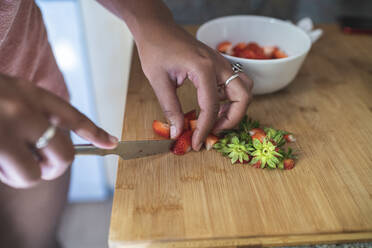 Nahaufnahme einer jungen Frau, die Erdbeeren auf einem Schneidebrett in der Küche zu Hause schneidet - SNF00500