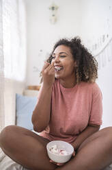 Happy young woman eating strawberries with cream while sitting at home - SNF00507