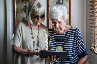Ältere weibliche Freunde benutzen ein digitales Tablet, während sie zu Hause stehen - DLTSF01027