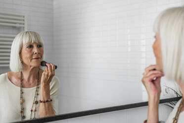 Ältere Frau trägt Make-up auf, während sie zu Hause in den Spiegel schaut - DLTSF01041