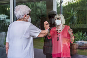 Senior woman visiting female friend through house window during curfew - DLTSF01061