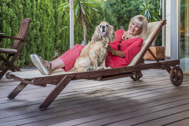 Stilvolle ältere Frau mit Hund entspannt auf Liegestuhl im Innenhof - DLTSF01066
