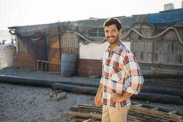 Lächelnder gutaussehender Mann, der am Strand vor einem Bauwerk steht - MPPF01003