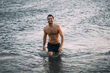 Shirtless smiling mid adult man wading in sea during sunset - MPPF01010